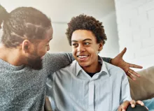 father with arm around son talking